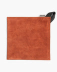 Terracotta suede leather hot pad with a black hanging strap on a white background
