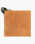 Tan suede leather hot pad with a black hanging strap on a white background