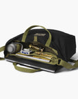 Black tote bag with green straps containing various items on a white background