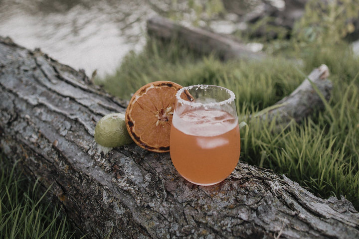 Grapefruit margarita in a wine tumbler on log by the river.
