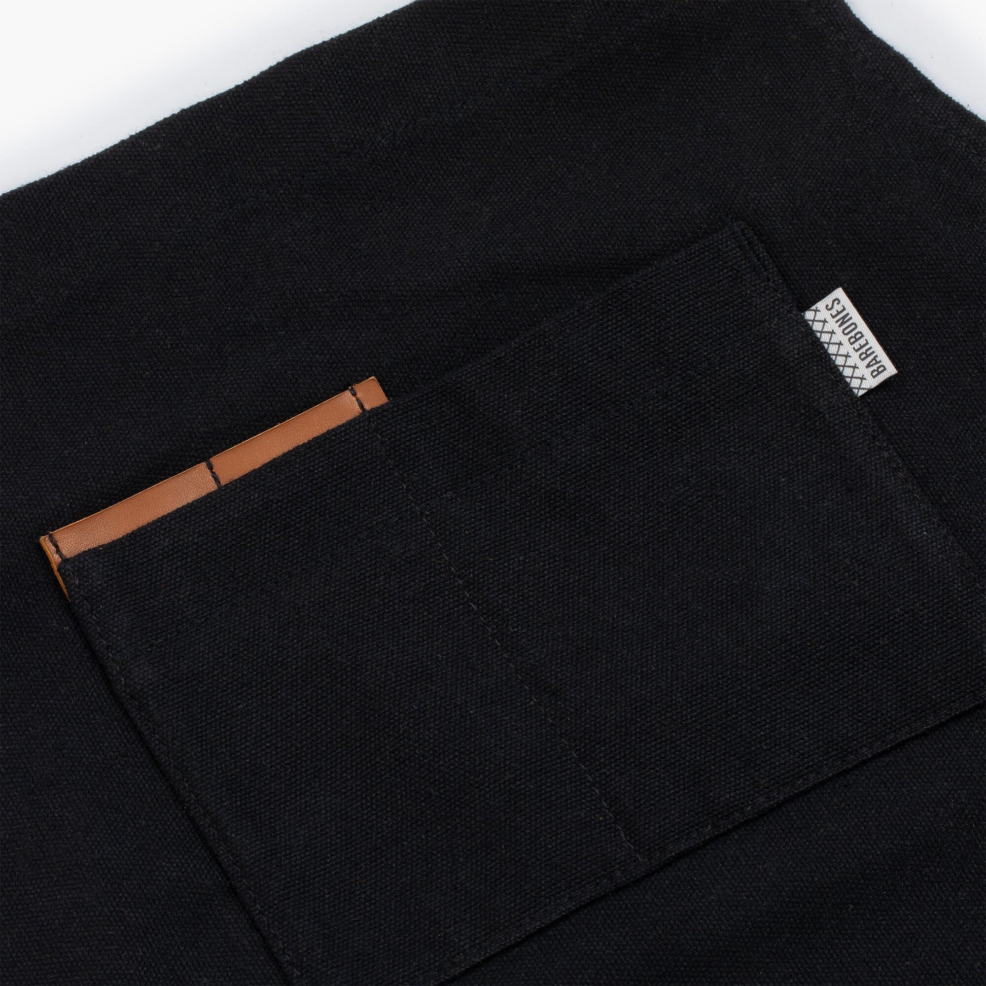 Close-up of a chest pocket on an a black apron with brown leather pad.