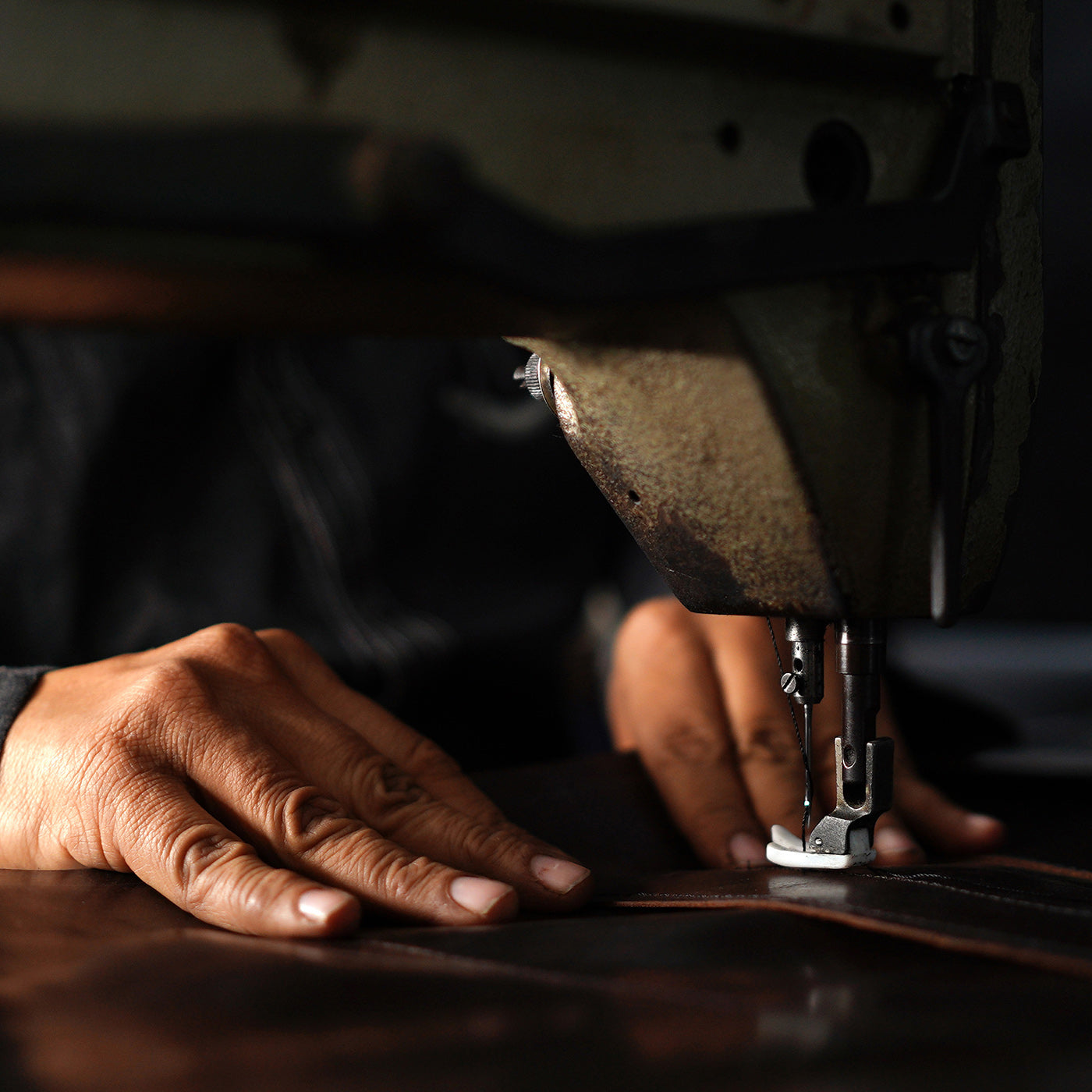 Close-up of a person's hands operating an industrial sewing machine on a dark background