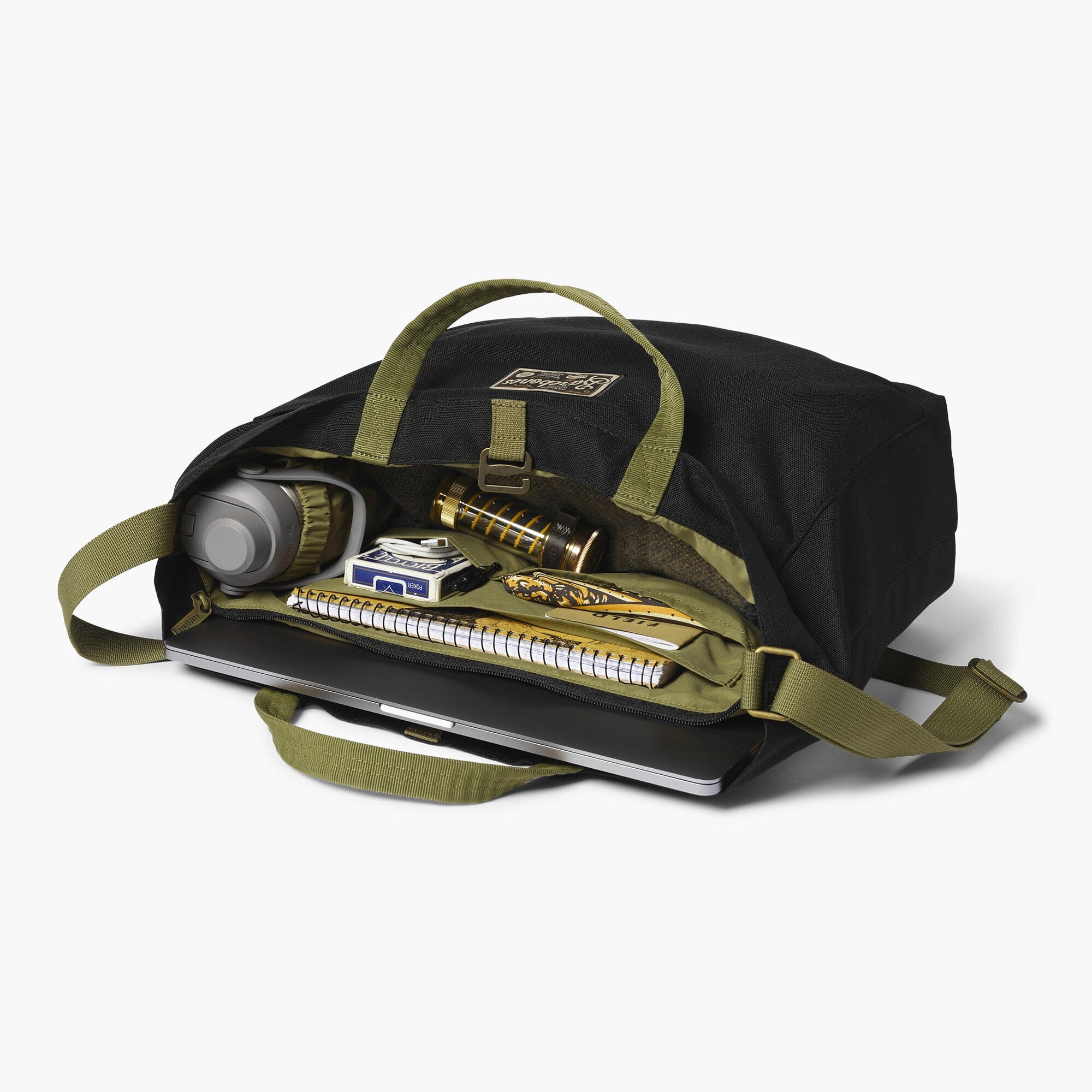 Black tote bag with green straps containing various items on a white background
