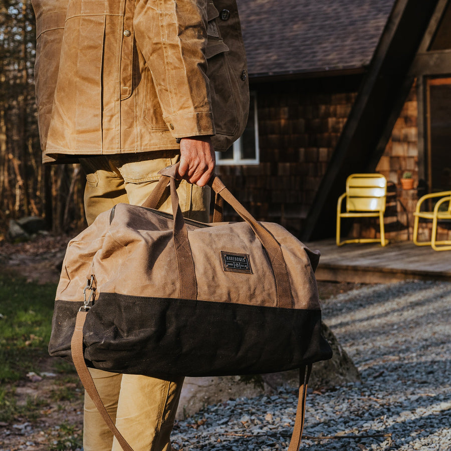 Man carrying a waxed canvas duffel bag to a cabin